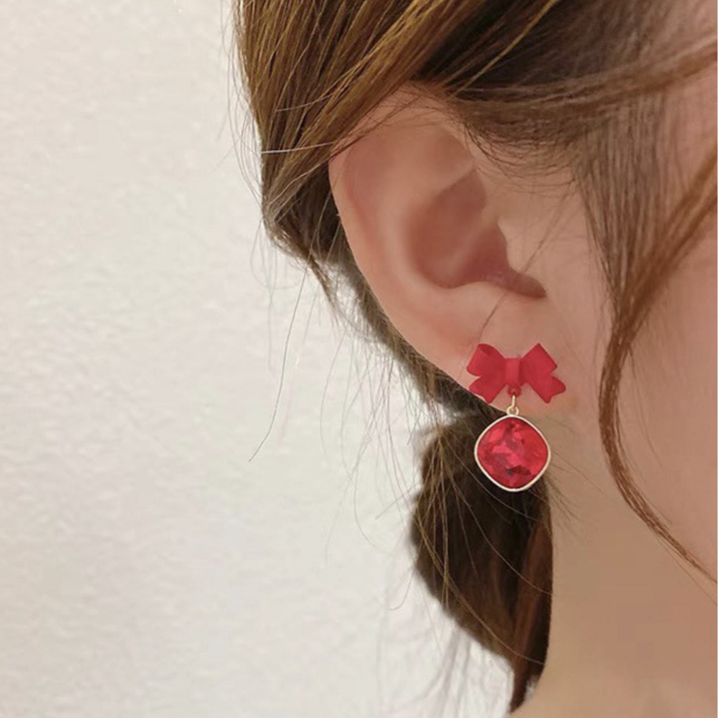 Red bow-shaped earrings worn by a person with a neutral background