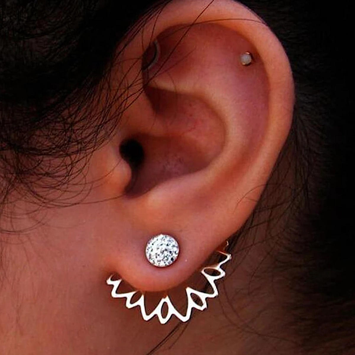 Gold-tone lotus ear jacket worn beneath a round crystal stud, ear close-up