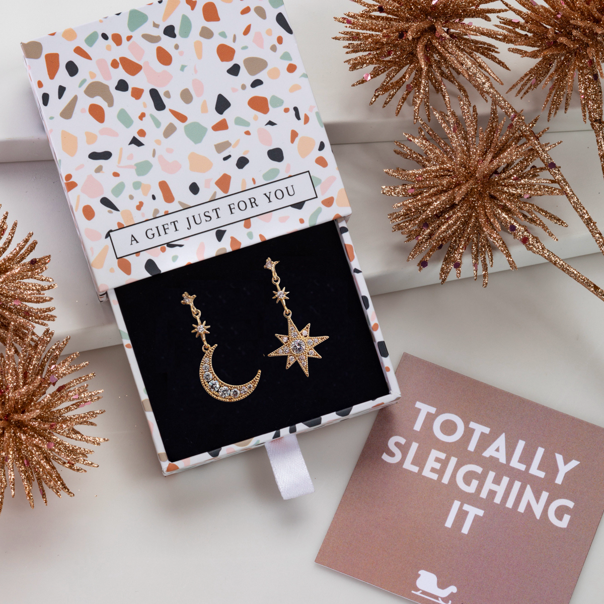 Asymmetrical cubic zirconia moon and star earrings in a patterned gift box with festive styling
