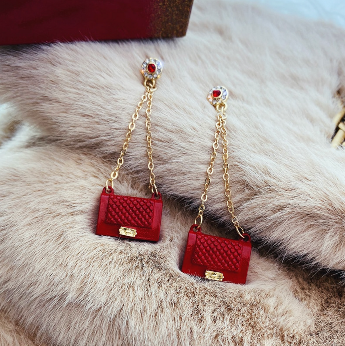 A pair of red and goldtone crystal-accent fashion clutch chain drop earrings displayed on a white surface with a furry texture.