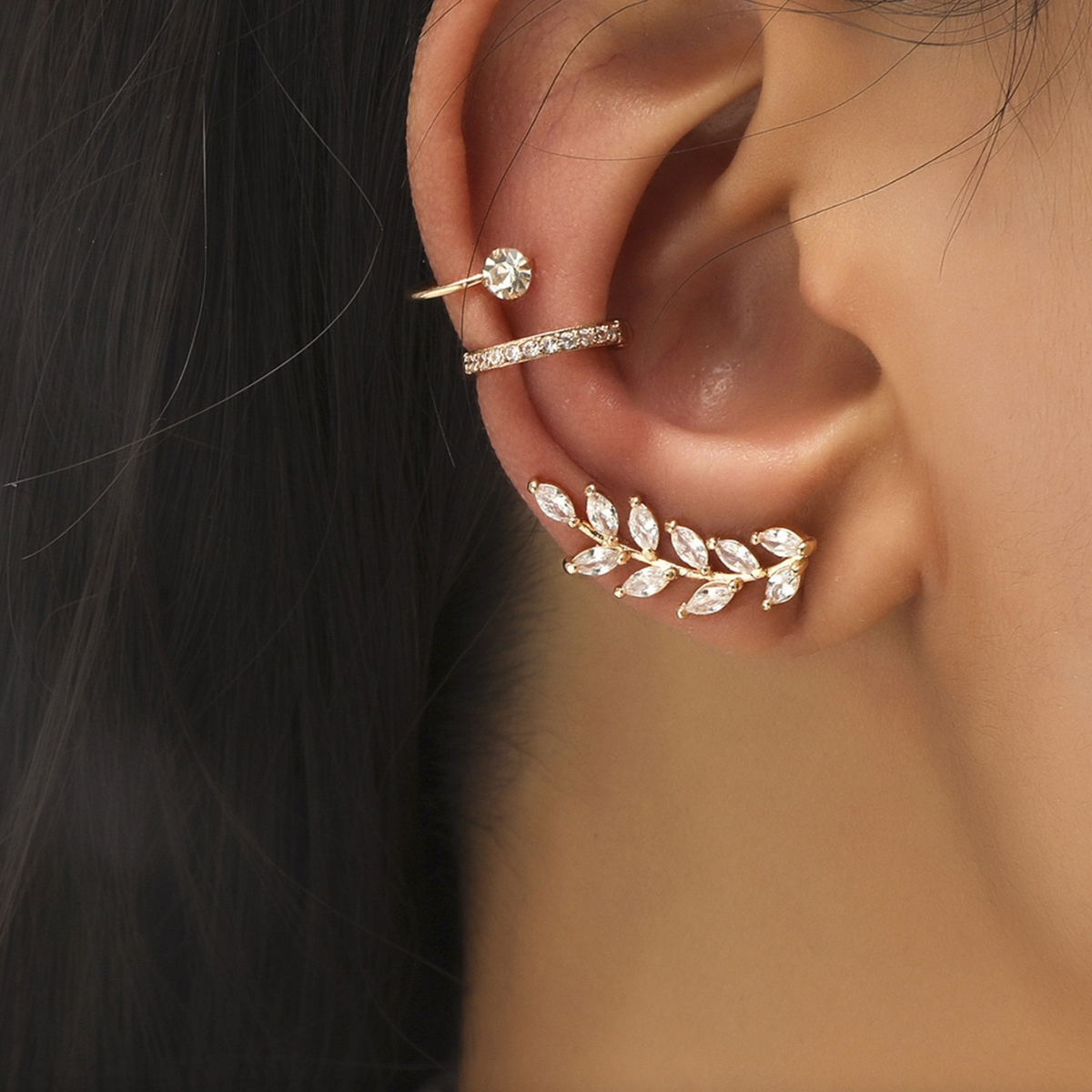 Model wearing a goldtone crystal leaf ear crawler and two crystal hoop ear cuffs