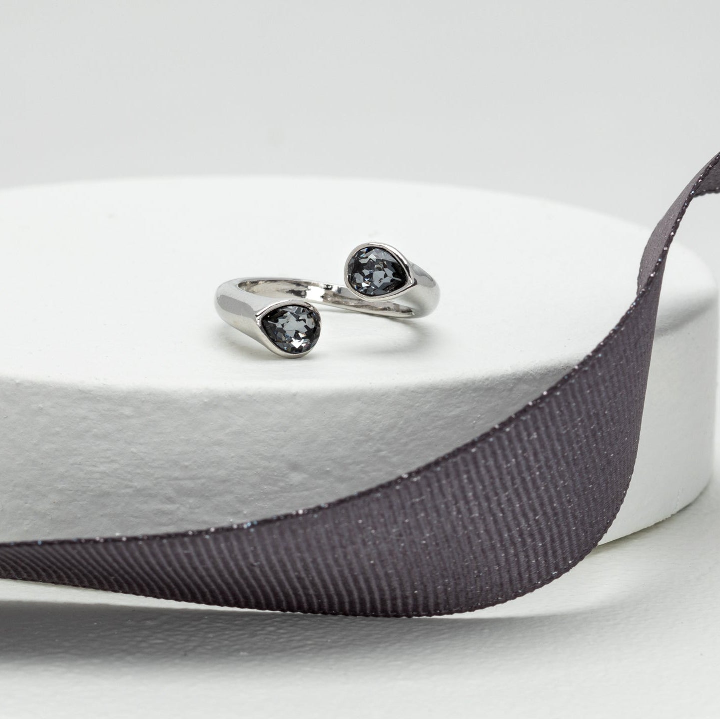 Elegant rhodium ring with pear-shaped Swarovski crystals, showcased on round display with dark ribbon accent