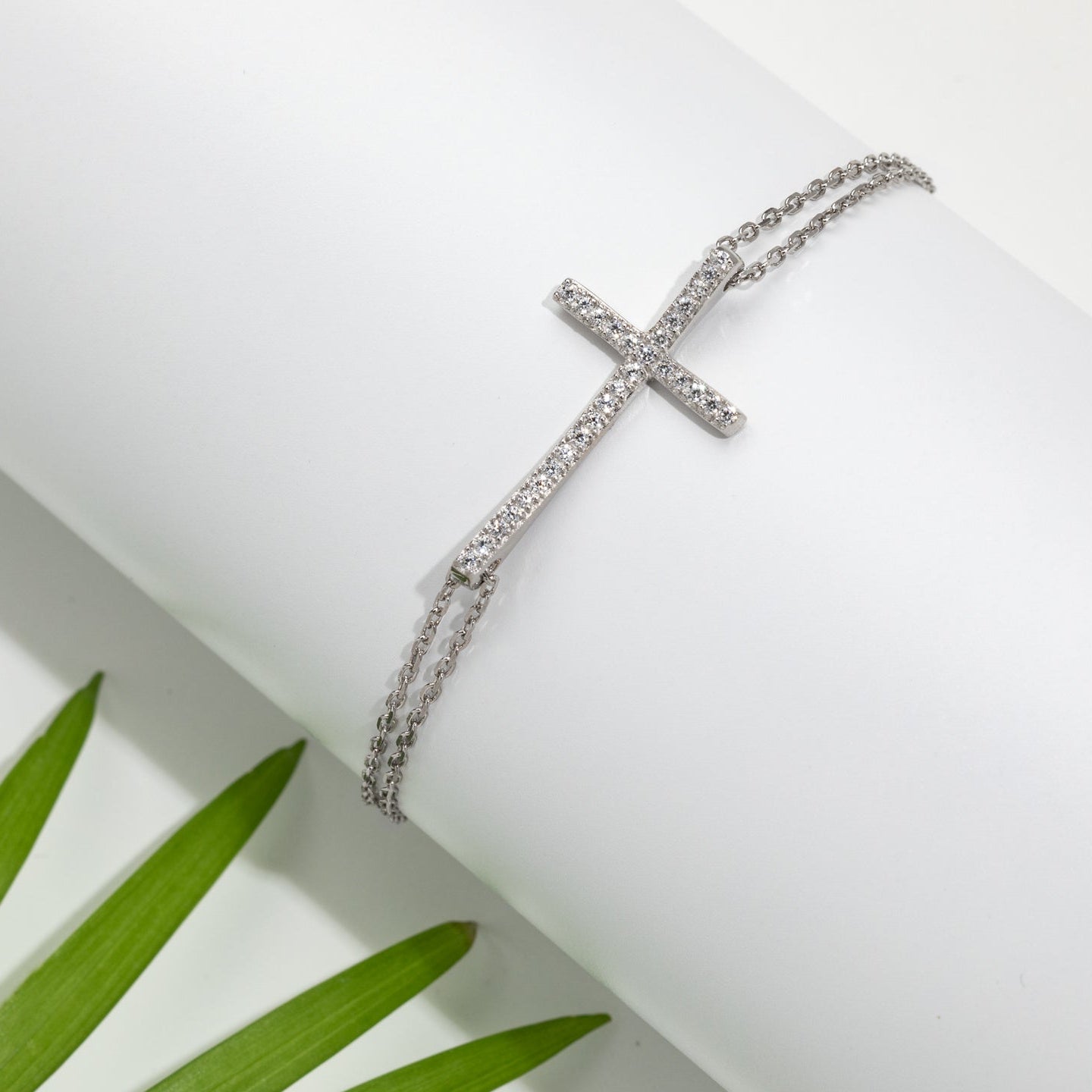 A sterling silver bracelet with cubic zirconia crosses, displayed on a white background with greenery in the background.