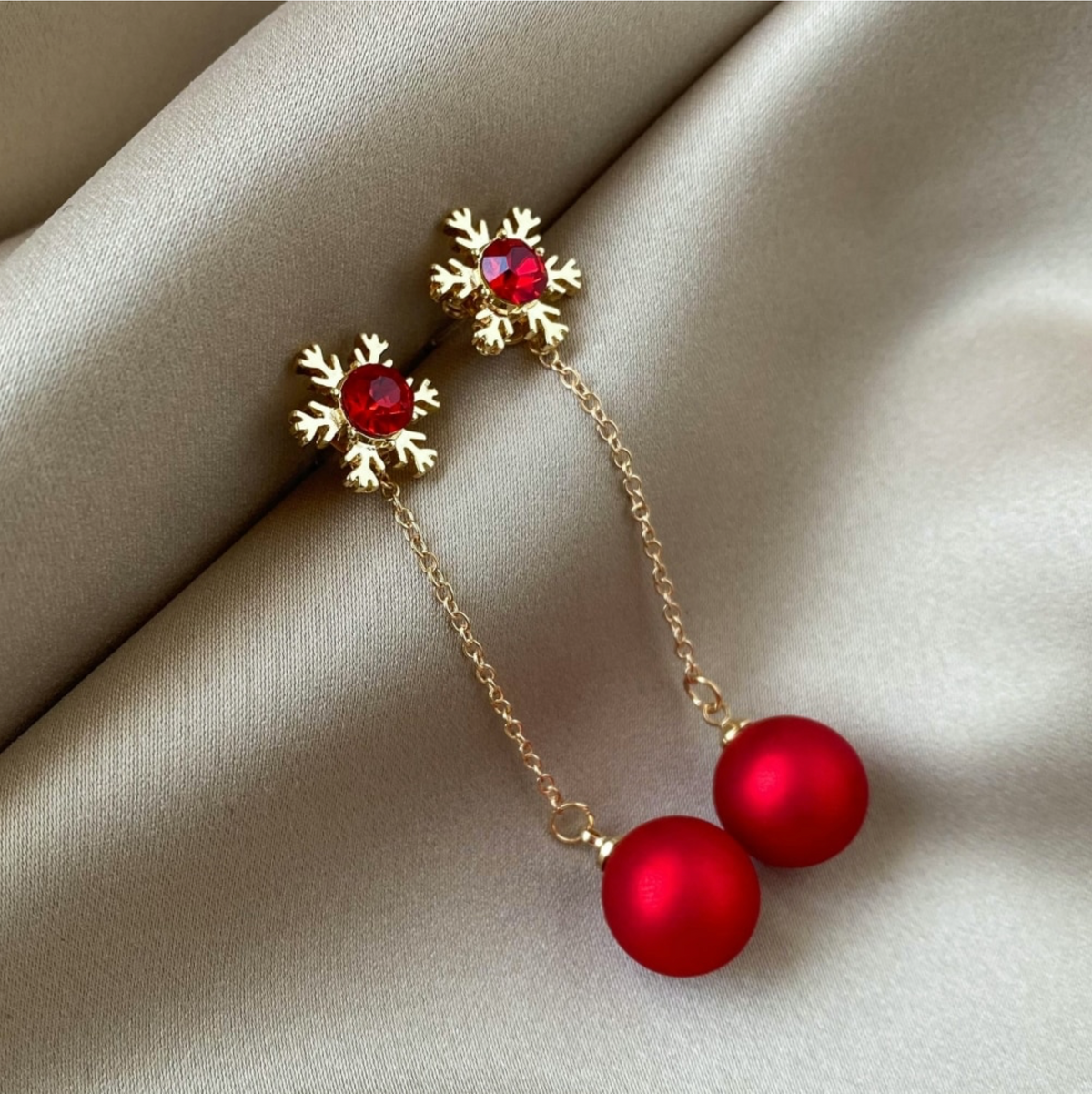 Goldtone red snowflake and bead drop earrings displayed on beige satin