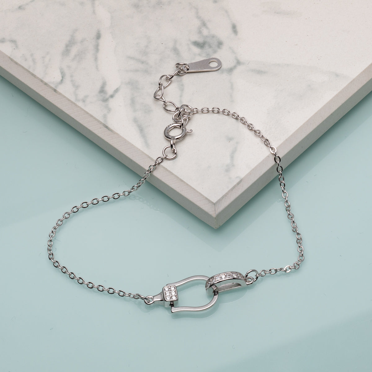 A sterling silver bracelet with a linked snaffle design and cubic zirconia stones, displayed against a marble background.