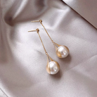A pair of goldtone earrings with imitation pearl drops, displayed on a silky fabric surface.