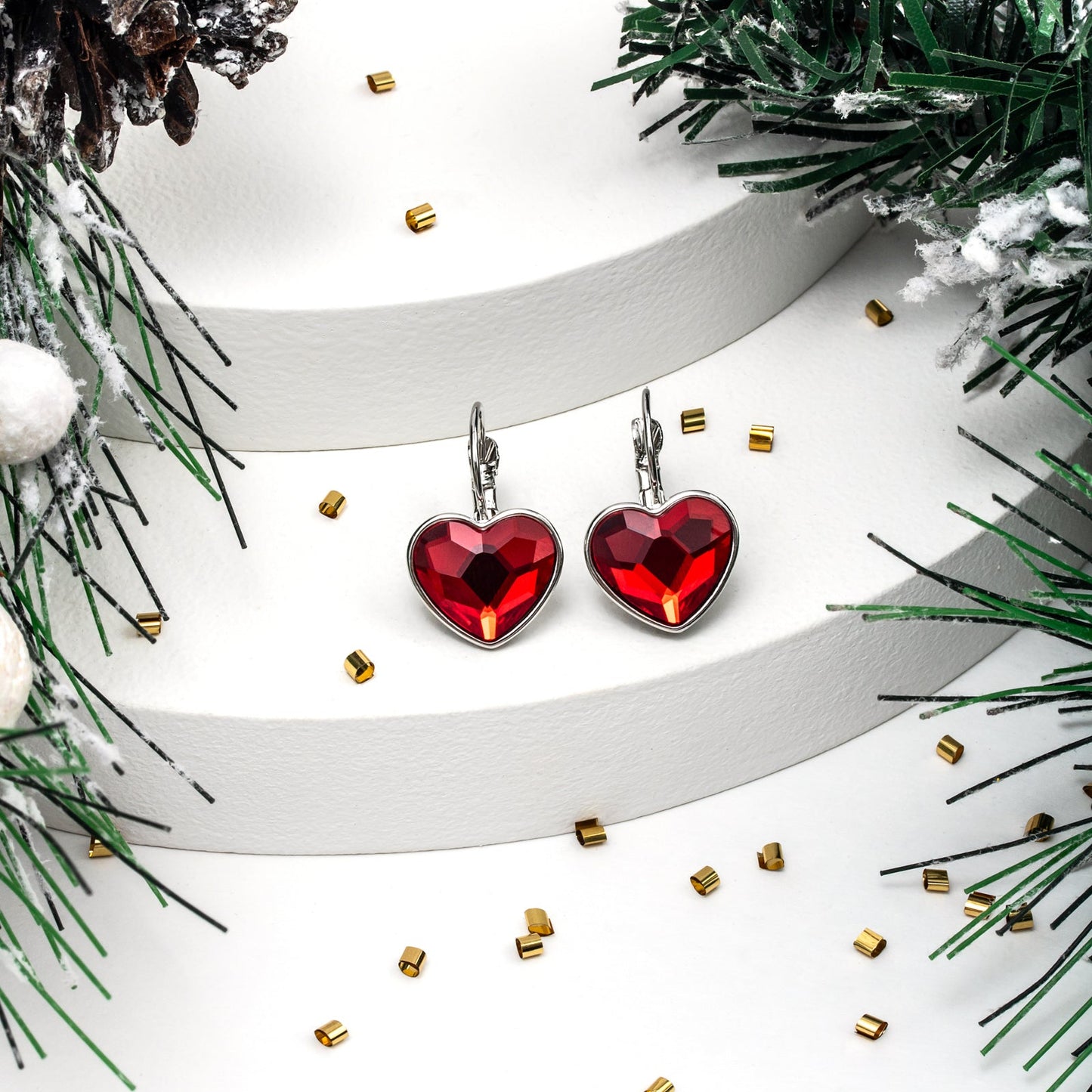 Red heart-shaped earrings on a white ribbon with greenery and gold accents