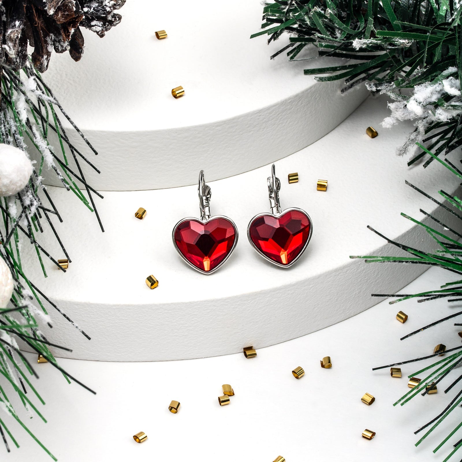 Red heart-shaped earrings on a white ribbon with greenery and gold accents