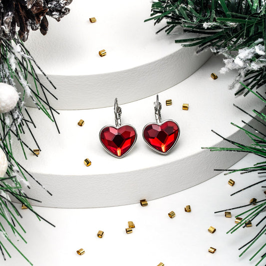 Red heart-shaped earrings on a white ribbon with greenery and gold accents