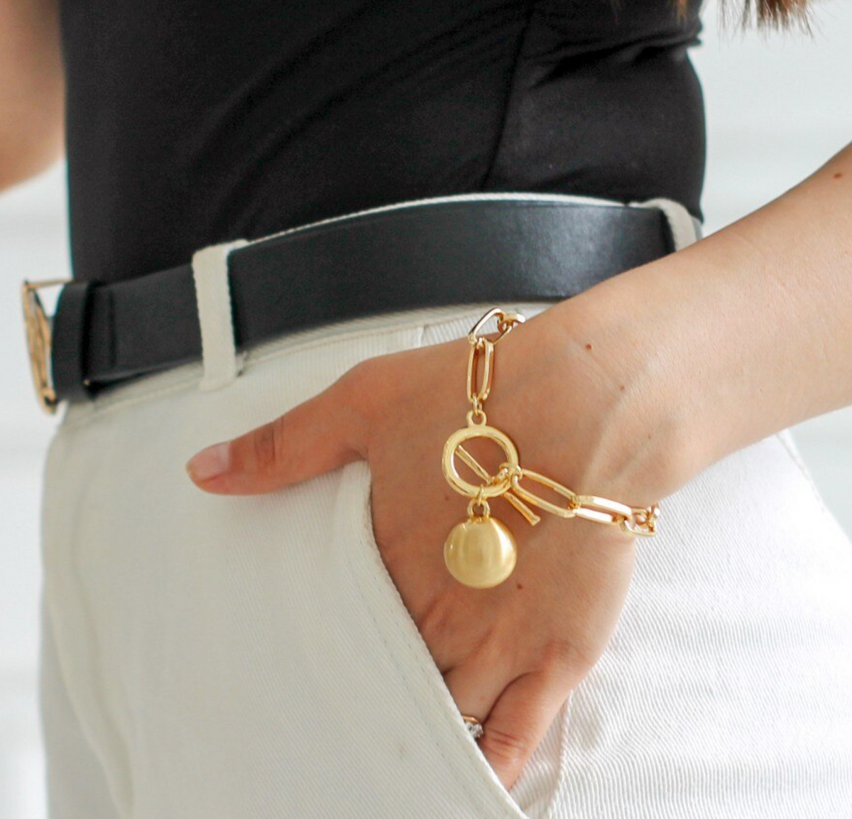 Model wearing a goldtone toggle bracelet with a ball charm