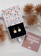 Gold-tone crystal floral earrings in a patterned gift box beside a pink card