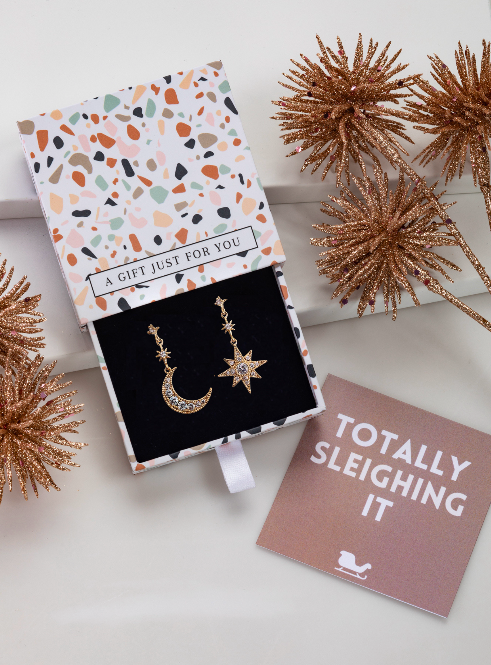 Asymmetrical cubic zirconia moon and star earrings in a patterned gift box with festive styling