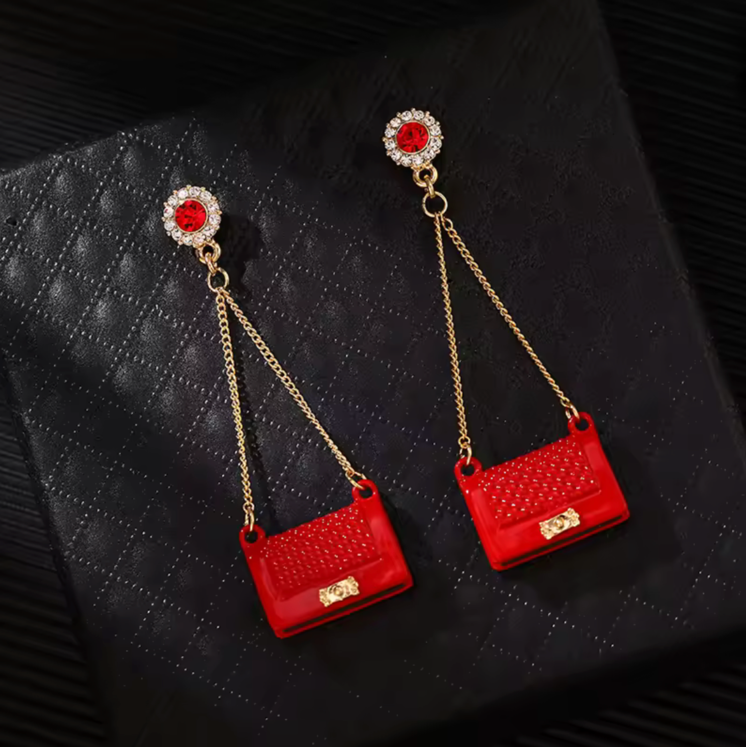 Red purse-shaped earrings with gold chains on a dark textured background