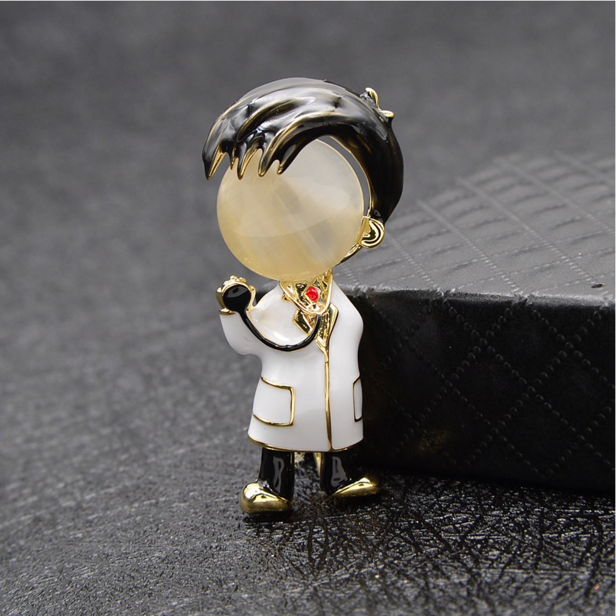 Doctor figure enamel brooch with a white coat displayed on a dark surface