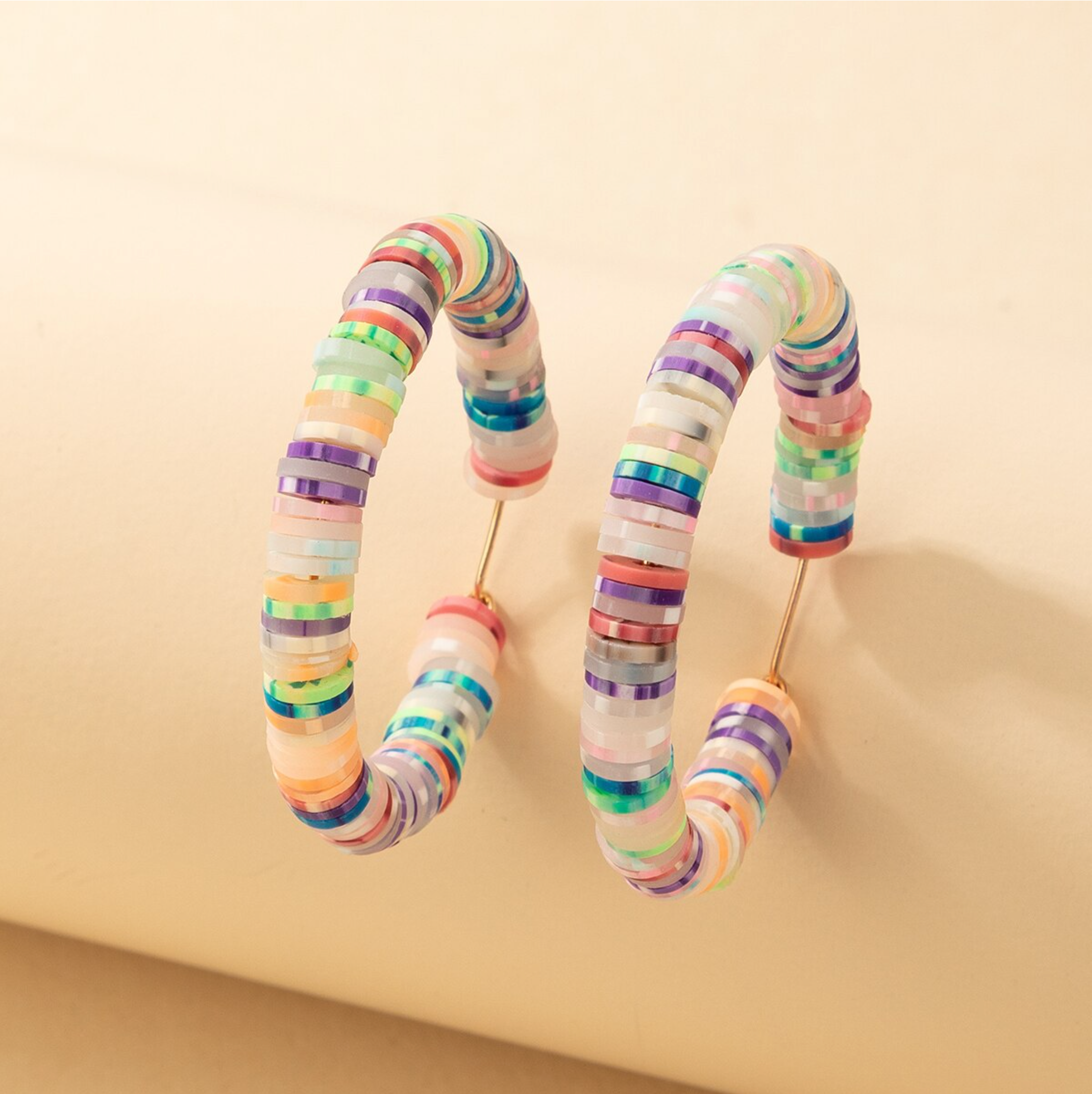 Multicoloured beaded hoop earrings standing on a peach display block
