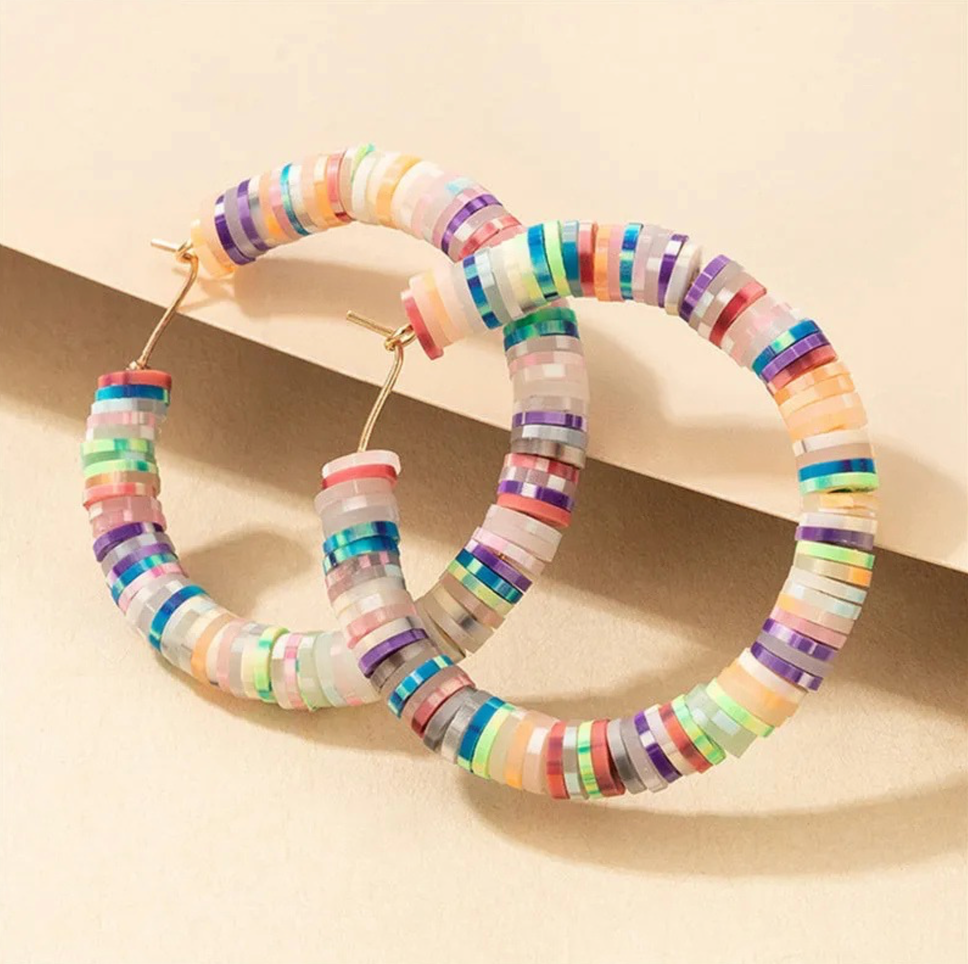 Rainbow-coloured beaded hoops, angled close-up on a peach block