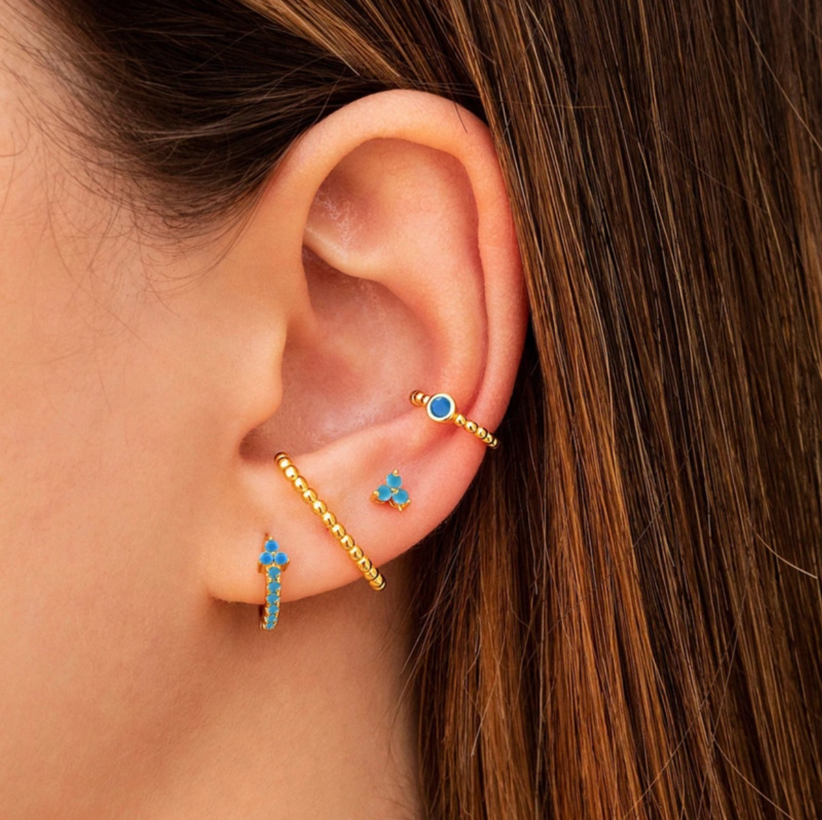 Model wearing gold-tone and blue crystal hoop, stud and ear cuff jewellery