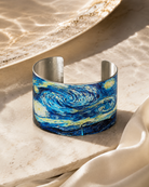 Blue swirling night-sky cuff bracelet displayed on a pale stone surface
