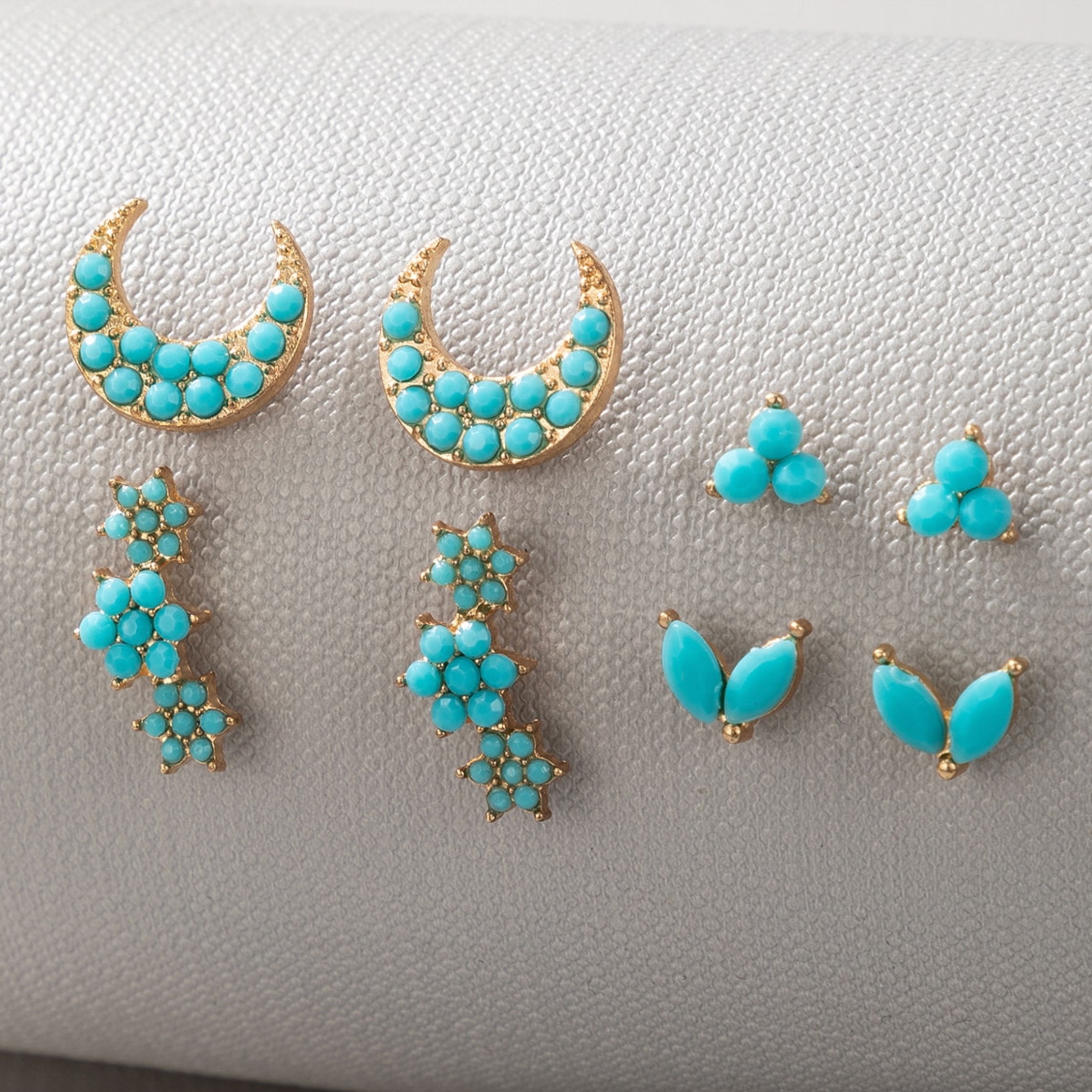 Turquoise-colored goldtone stud earrings displayed on white fabric