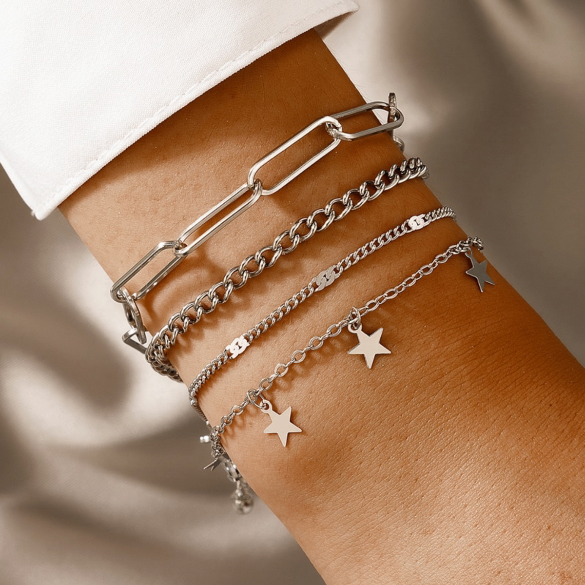 Four silver-tone chain bracelets with paperclip links and dangling stars, worn on a wrist