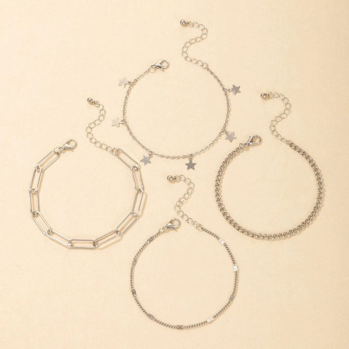 Four silver-tone chain bracelets arranged separately on a beige background