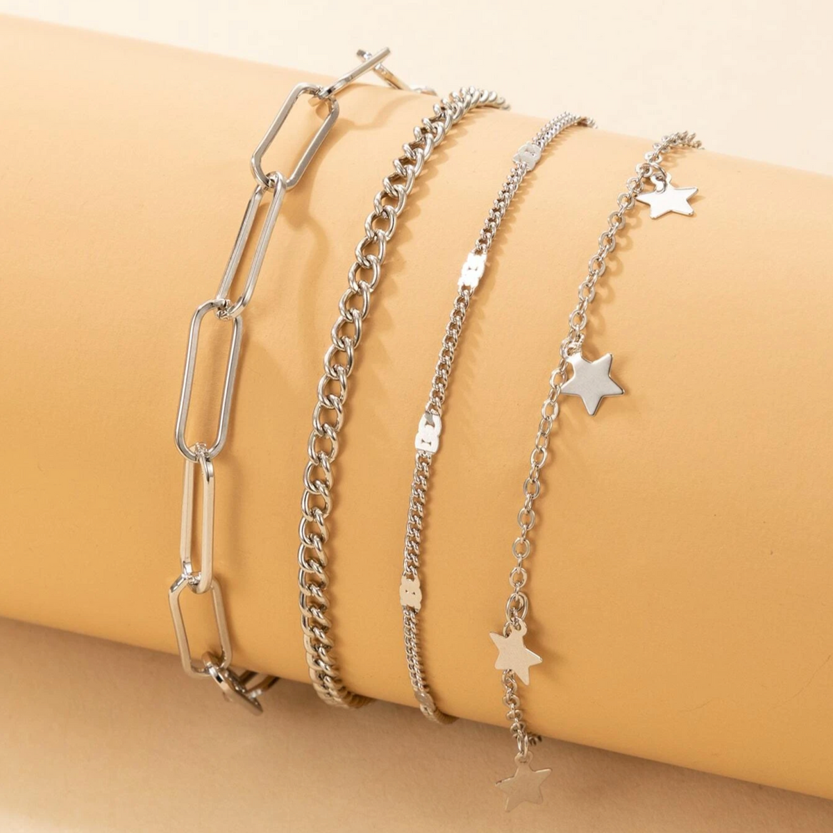Four silver-tone bracelets with mixed chain links and star charms on a yellow display
