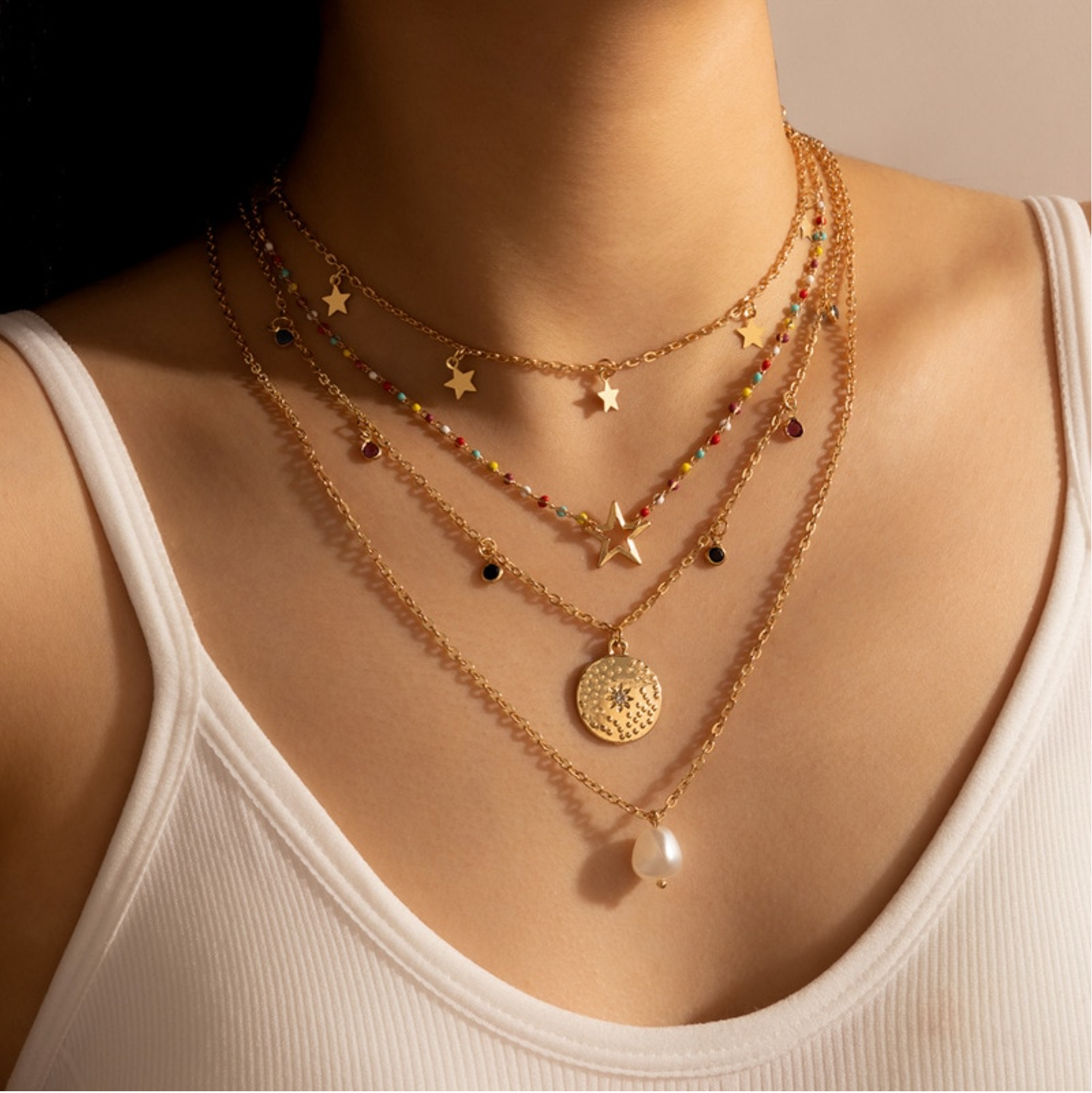 Model wearing a gold-tone layered charm necklace with a white faux pearl drop