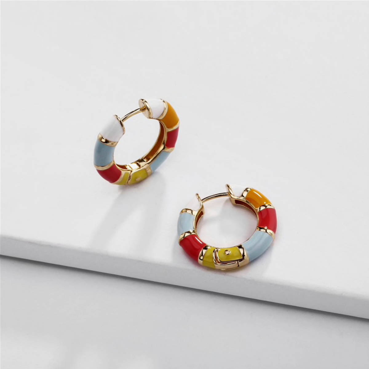 Small multicoloured huggie hoop earrings displayed on a white block