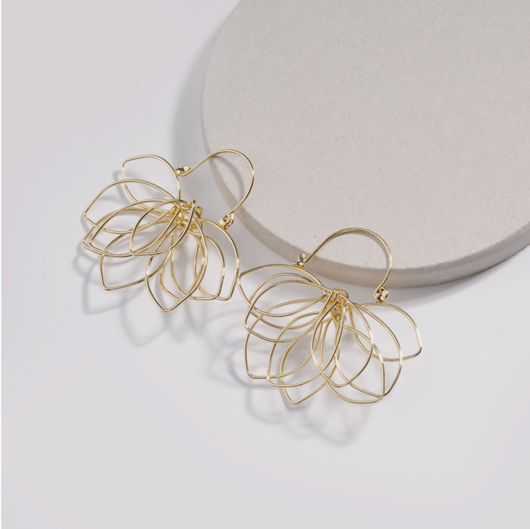 Gold-tone openwork lotus flower earrings displayed on a white block