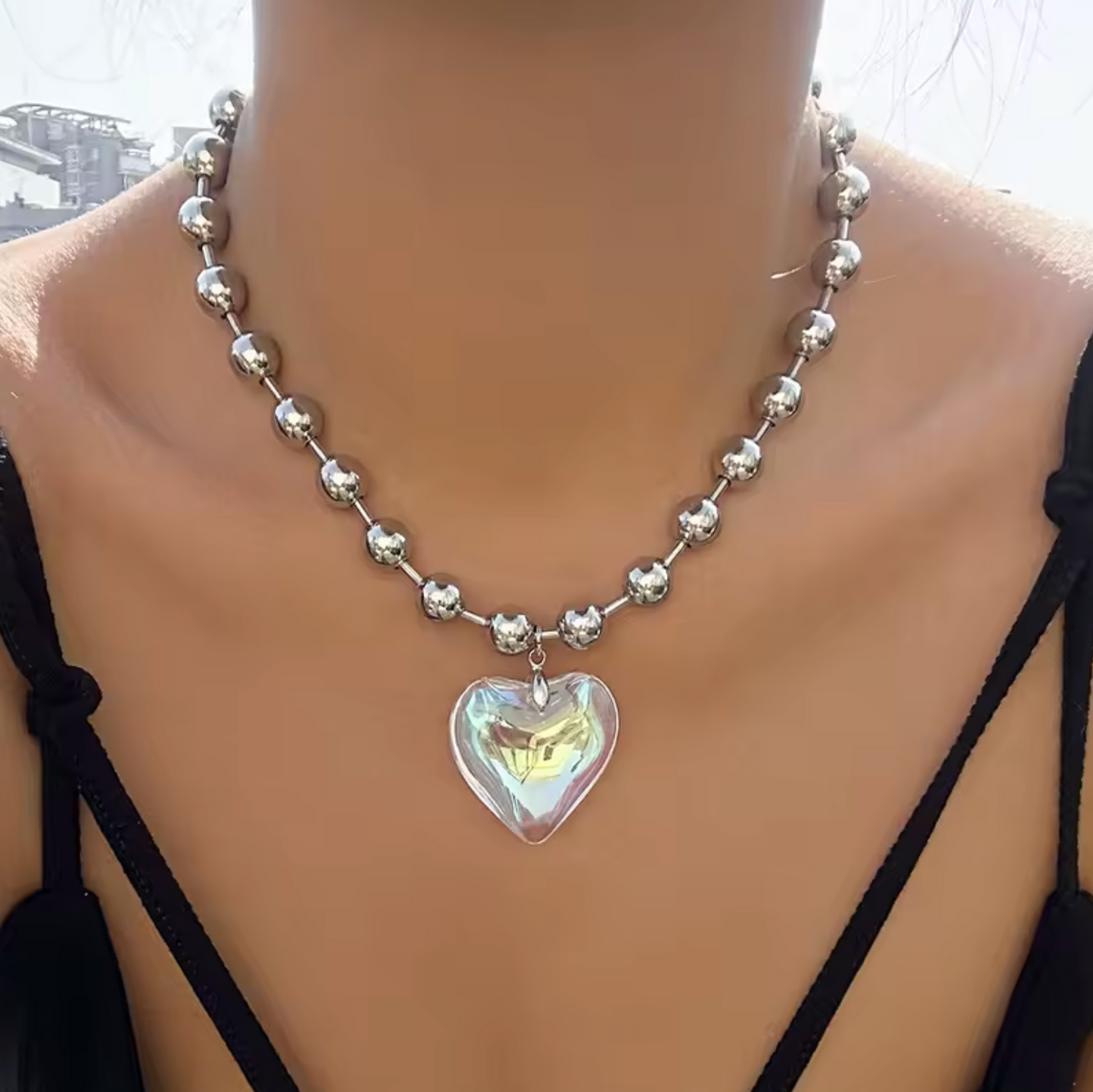 Silver beaded necklace with a heart-shaped pendant on a person wearing a black top.