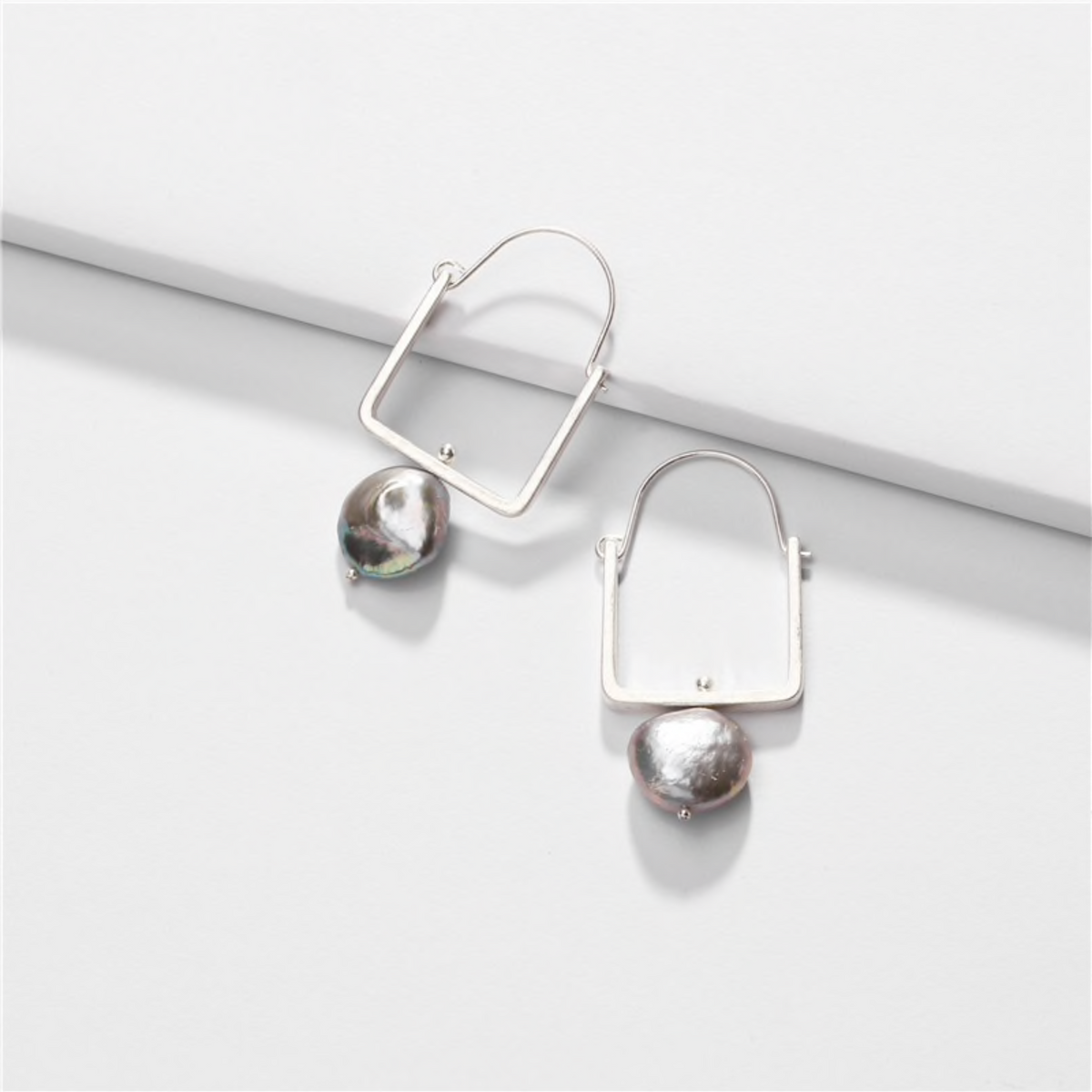Geometric silver-tone pearl earrings displayed on a white block