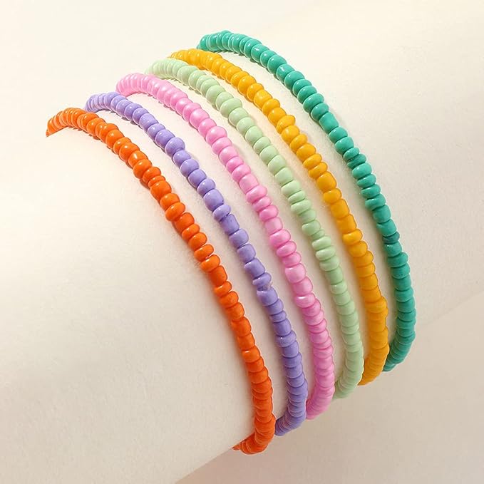 Rainbow seed bead anklets stacked on a white display