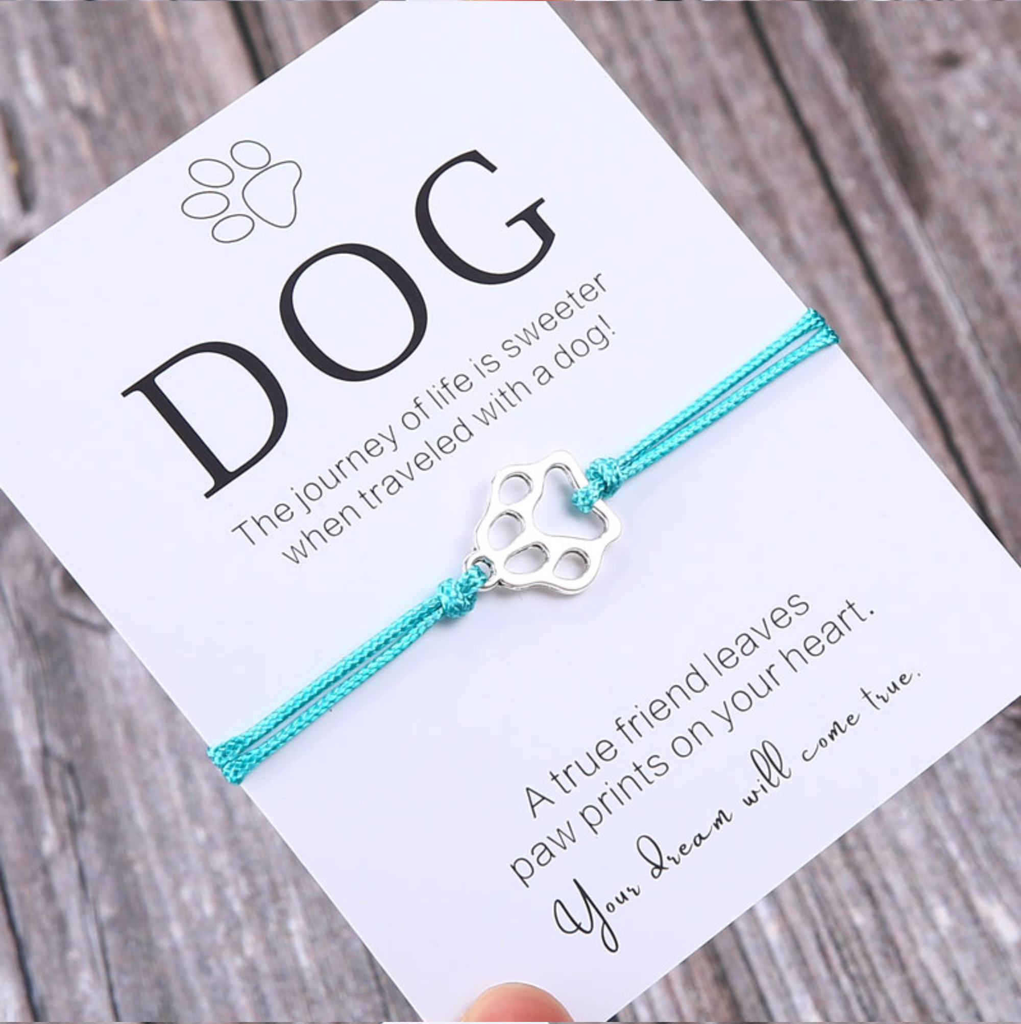Turquoise cord adjustable bracelet with a silvertone paw print charm on a dog message card