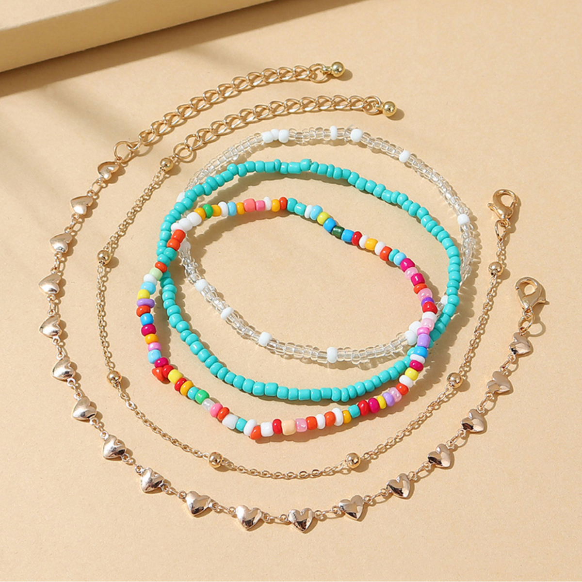Turquoise bead and silver-tone heart anklet set displayed on a peach background