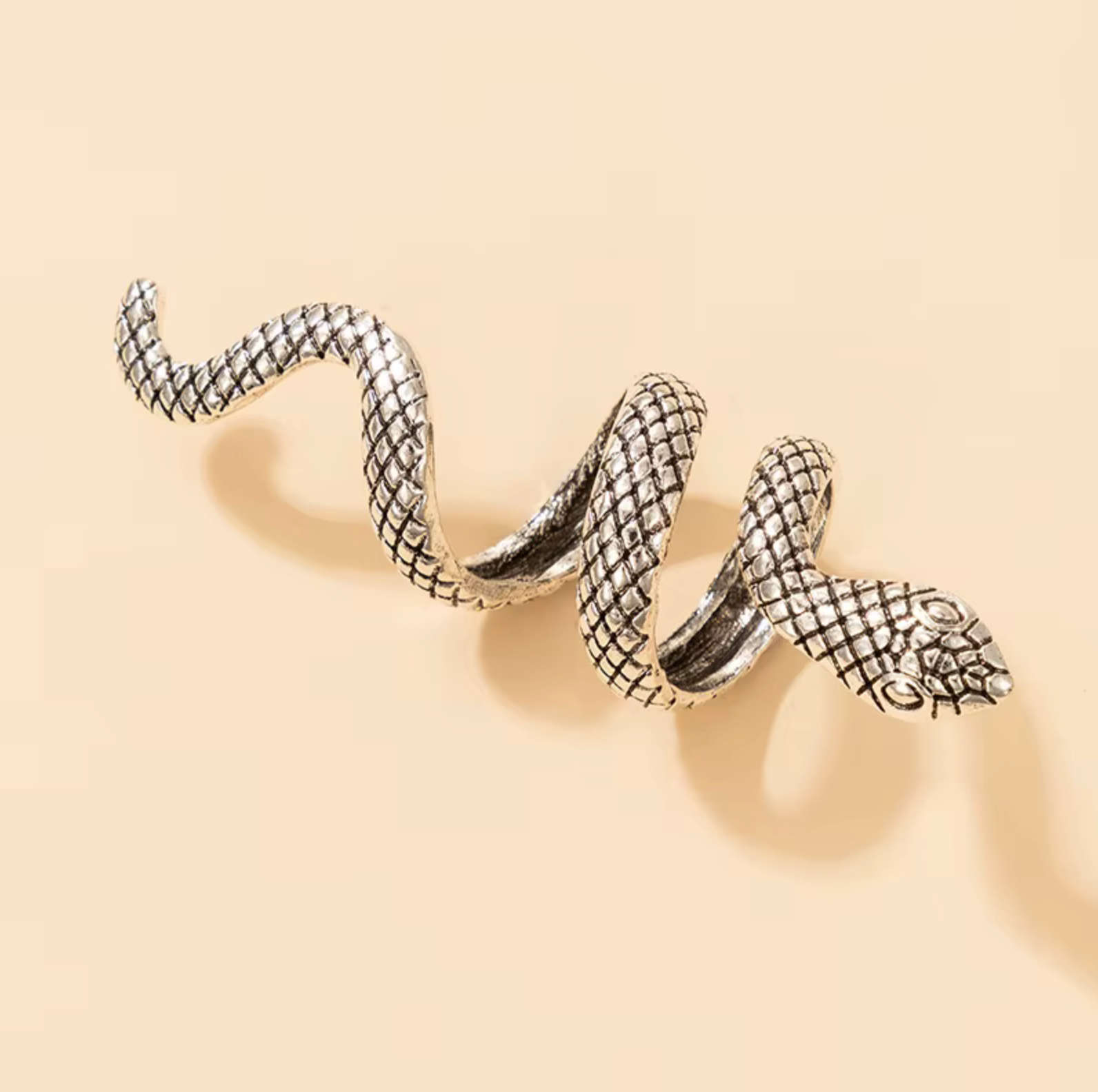 Long coiled snake ring with textured silver-tone scales on a peach background