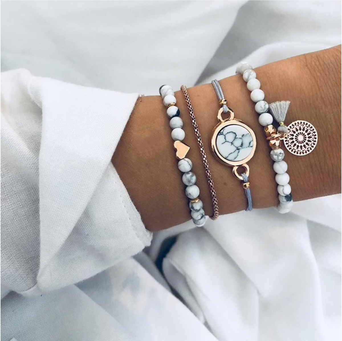 White howlite and rose gold-tone bracelet stack with round marbled centre, worn on a wrist