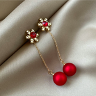 Goldtone red snowflake and bead drop earrings displayed on beige satin