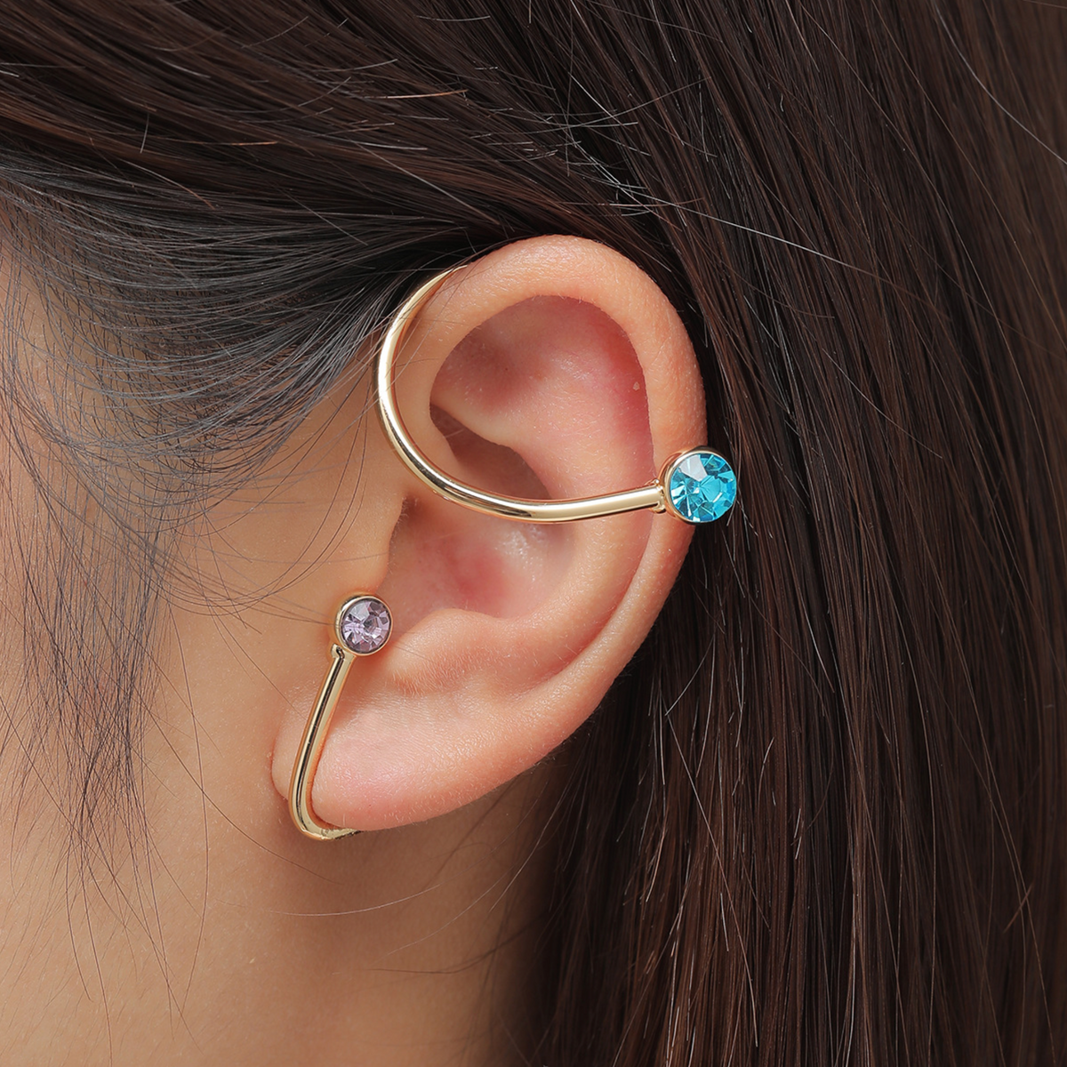 Gold-tone ear cuff with purple and aqua crystals, worn around an ear