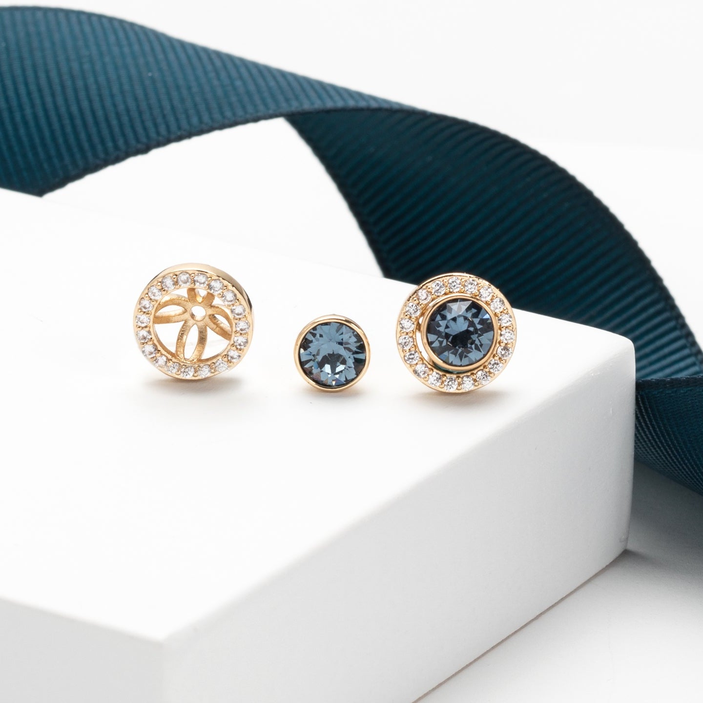 Gold earrings with gemstones on a white box with a blue ribbon