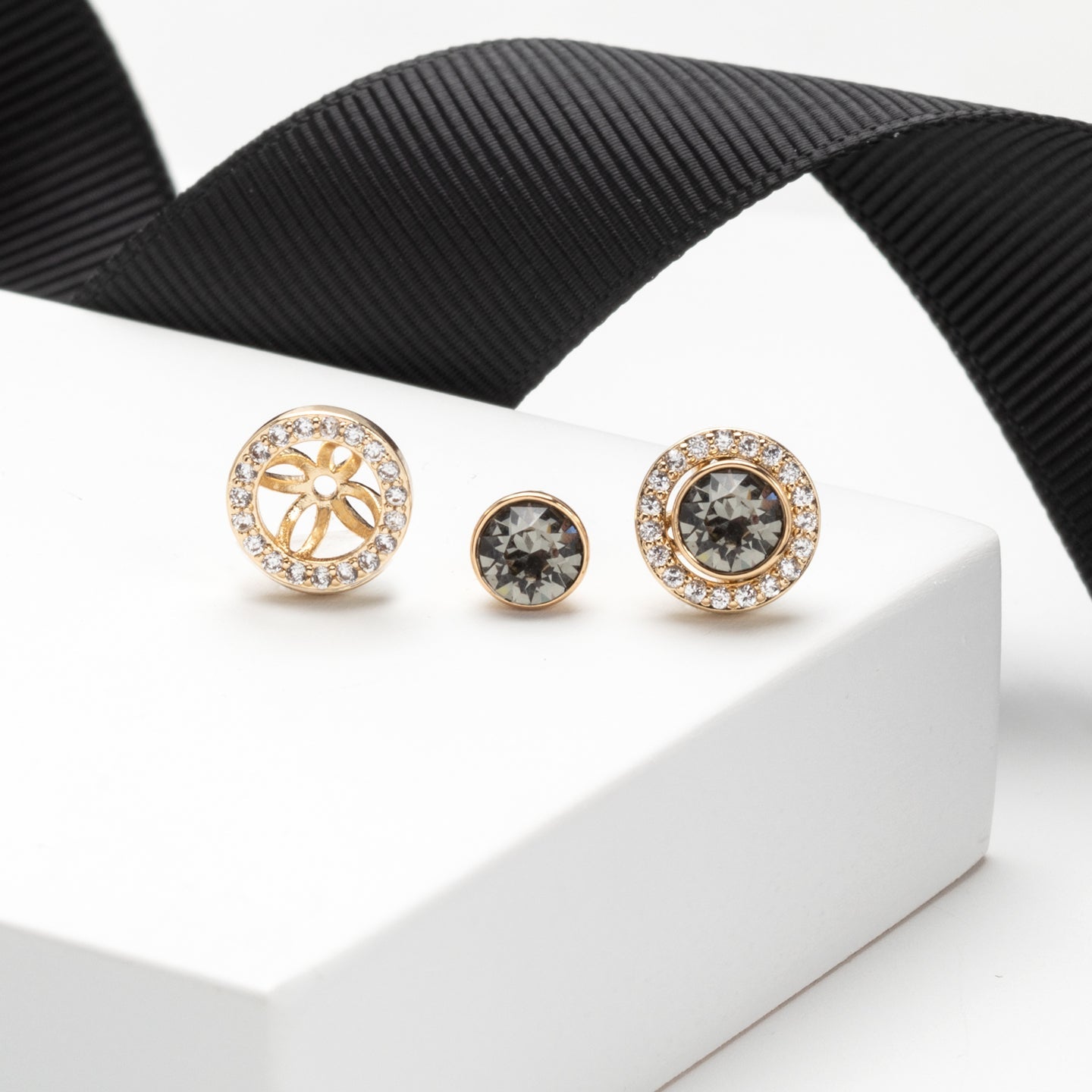 Pair of gold earrings with gemstones on a white stand with black ribbon