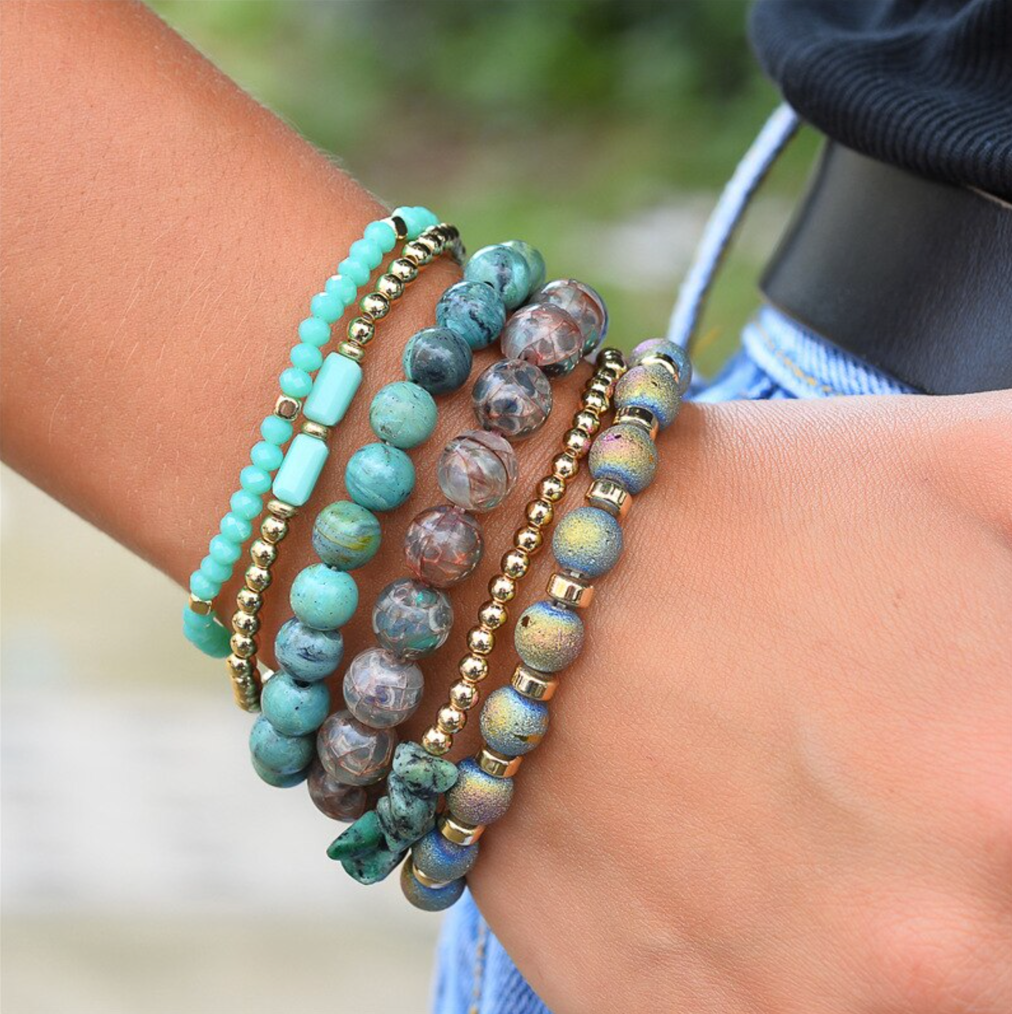 Close-up of a green, gray and gold-tone bead bracelet stack on a wrist