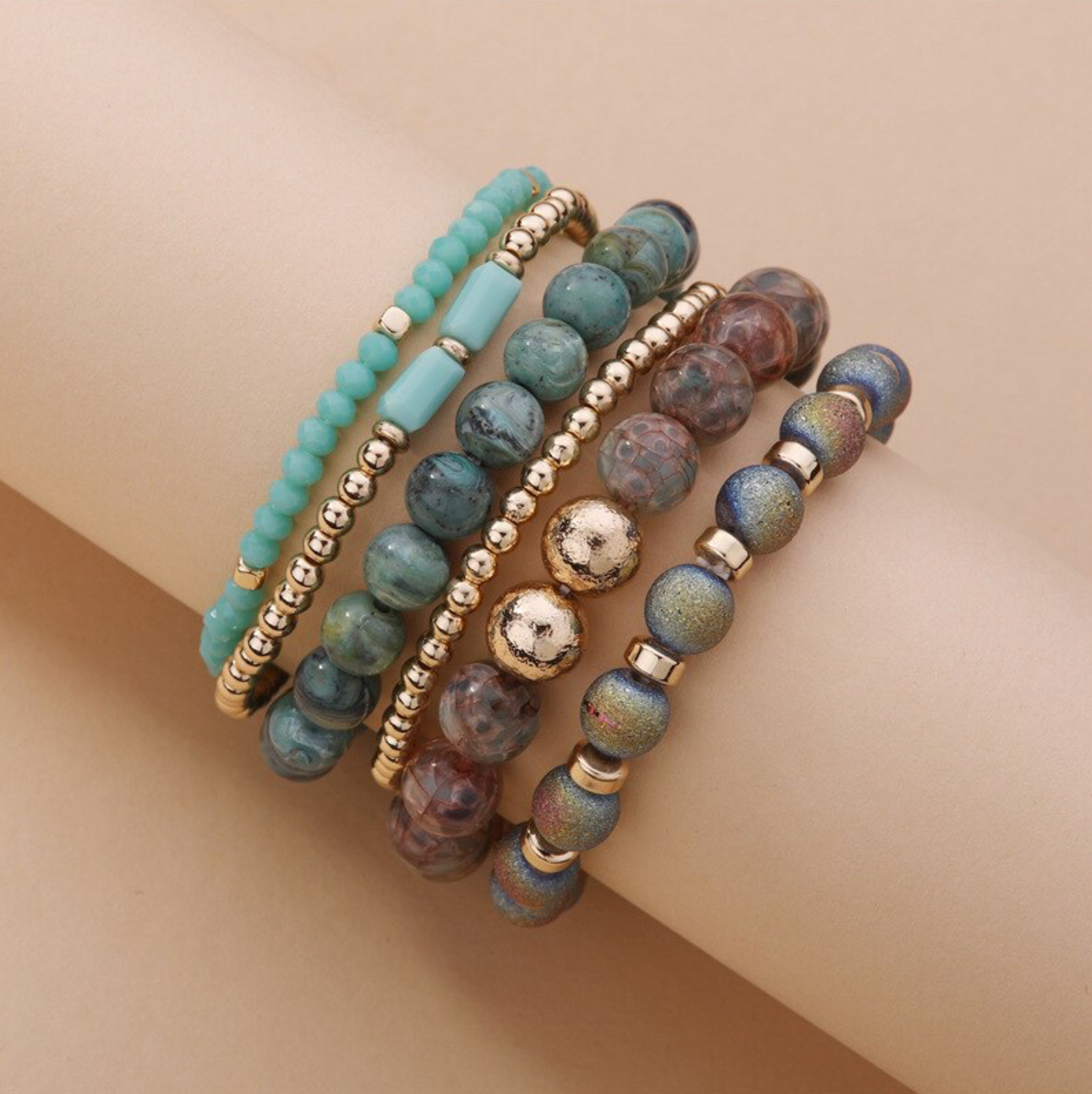Green, gray and gold-tone beaded bracelet stack displayed on a peach block