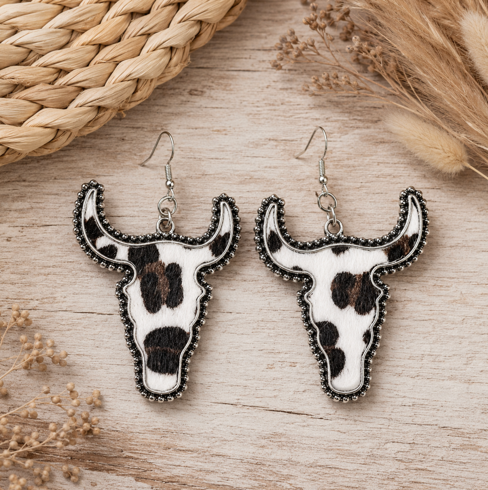 Black and white cow print longhorn earrings laid on a pale wood surface