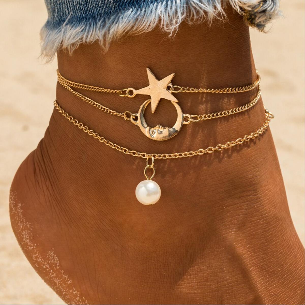 Three gold-tone anklets with star, crescent moon and white faux pearl charms, worn on an ankle