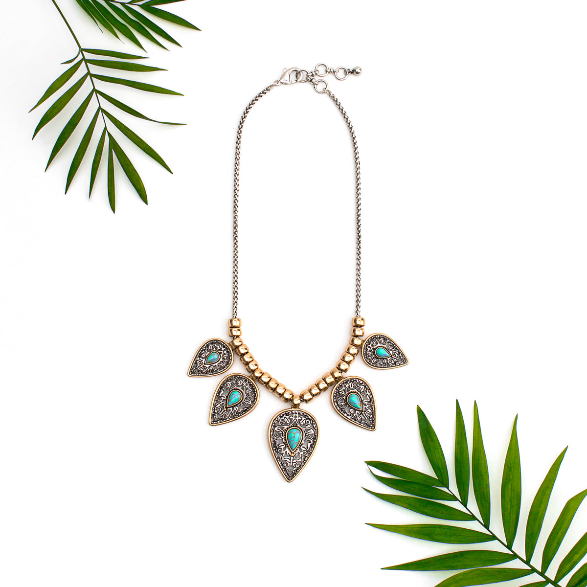 Teal leaf statement necklace displayed with green leaves