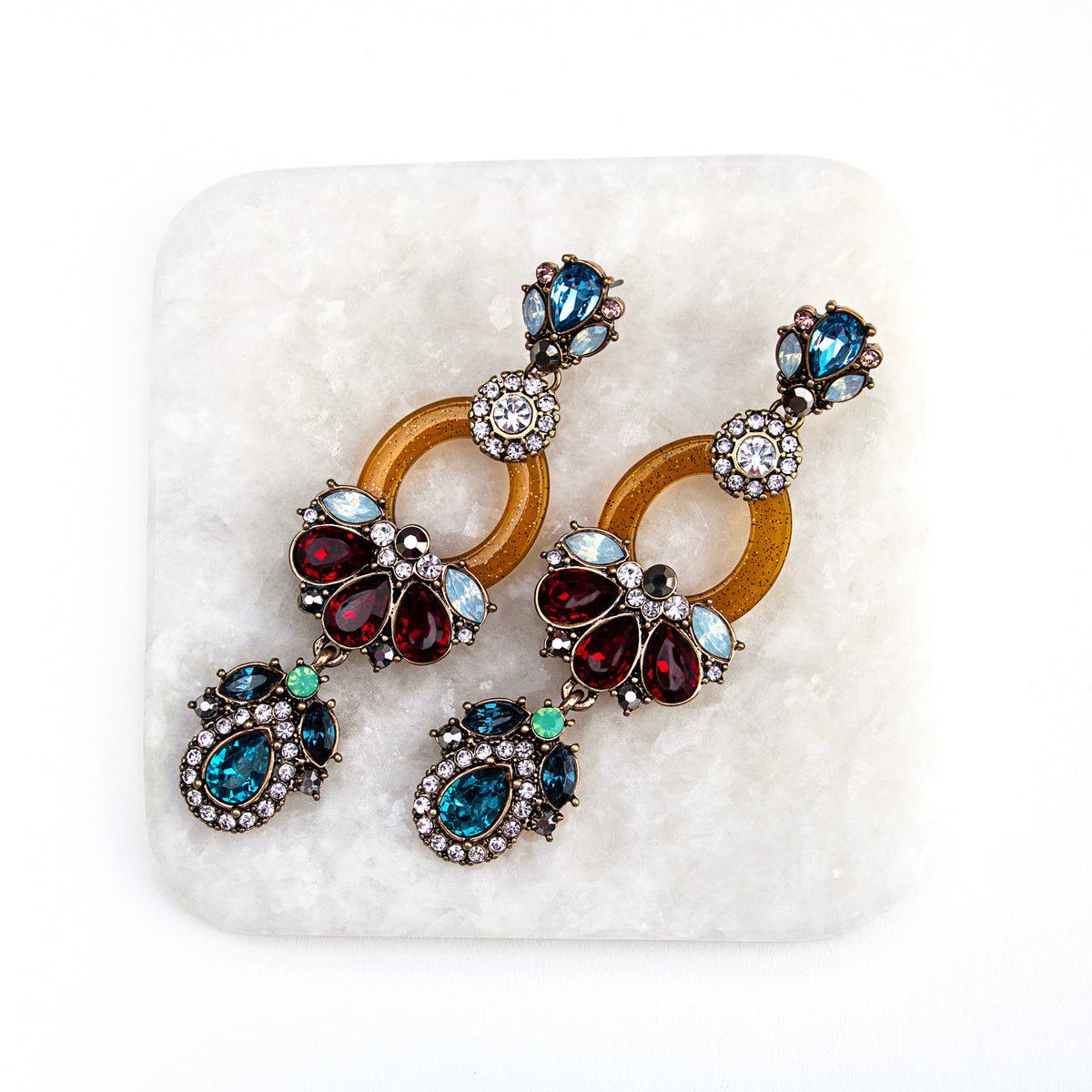 Multicoloured crystal statement earrings displayed on a white textured block