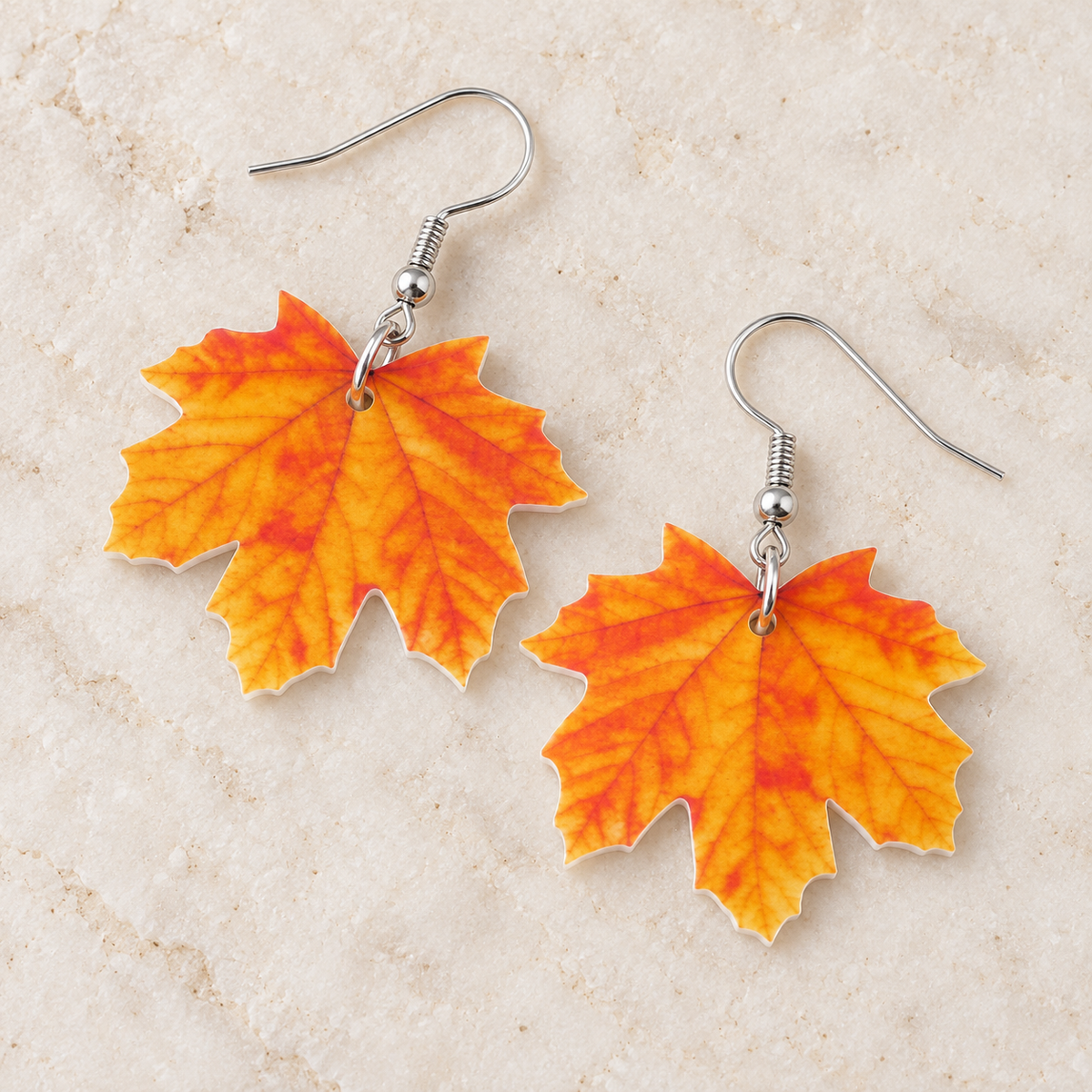 Orange and yellow maple leaf earrings arranged on an ivory stone surface