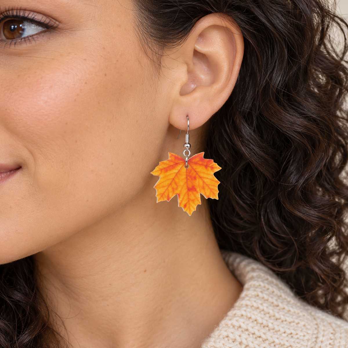Orange maple leaf drop earring worn by a model with dark curly hair