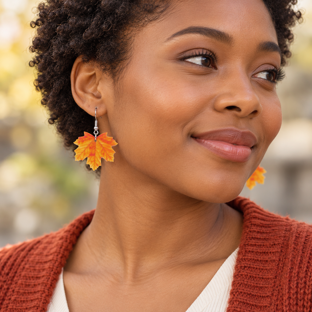 Orange autumn maple leaf earrings worn by a model in a rust cardigan