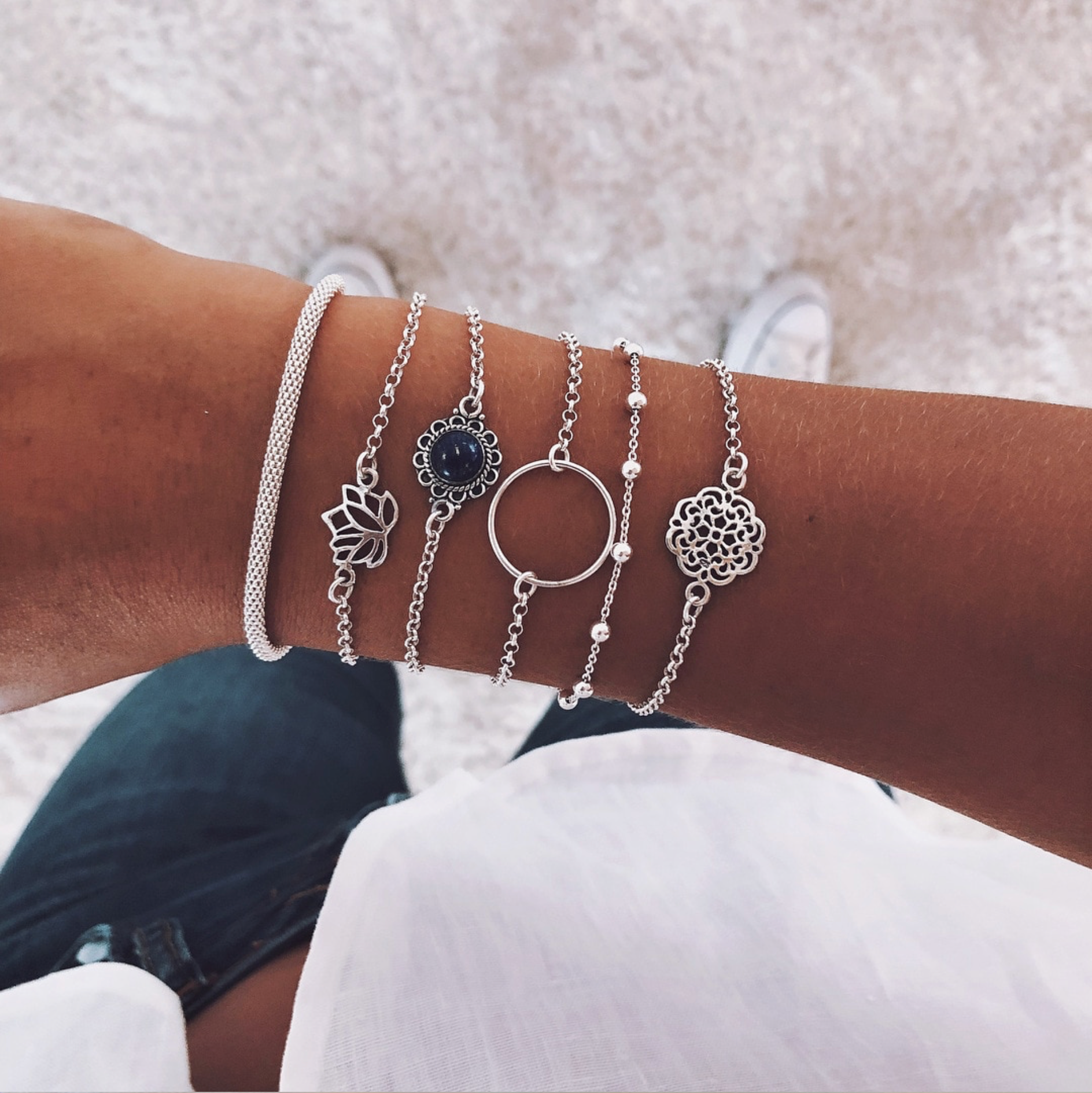 Silver-tone bracelet stack with lotus, open-circle and mandala charms, worn on a wrist